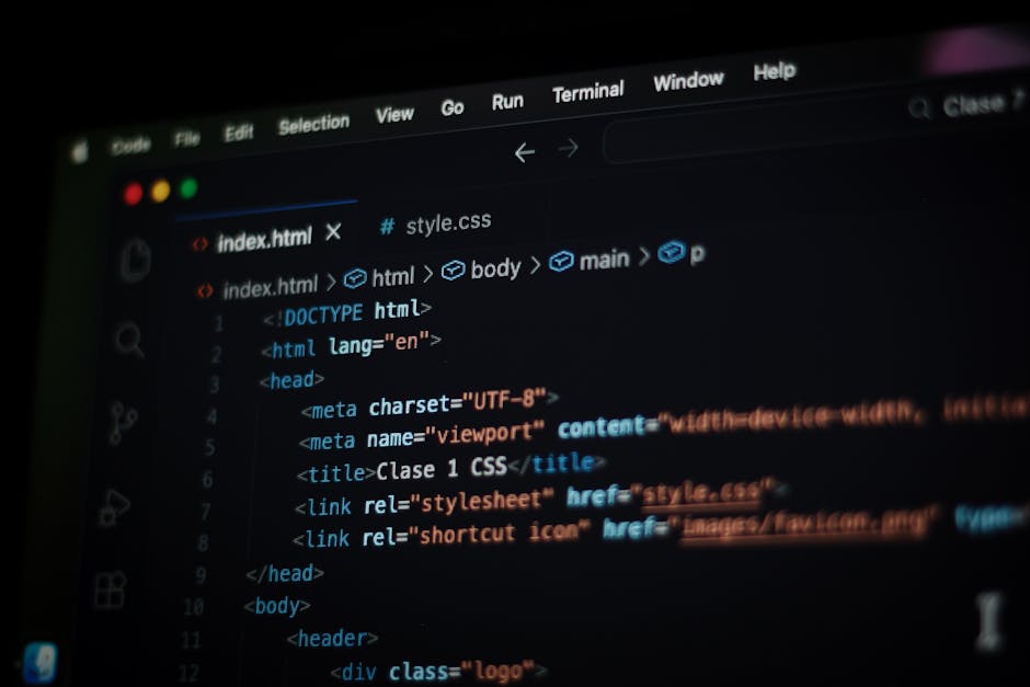 A close-up view of a person's hands operating a laptop on a dark table, displaying a code editor with colorful lines of programming code. The background is blurred, emphasizing the focus on the hands 